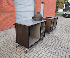 Vuurkorf en BBQ — BBQ-tafel met Kamado · Buitenleven · Sculpturale vuurkorf uit lasergesneden cortenstaal, optioneel met grillarm en hangende RVS rooster. Ook leverbaar als BBQ-tafel op wielen met RVS werkblad, houten front en uitsparing voor een Kamado of gasgrill — maatwerk per setup.